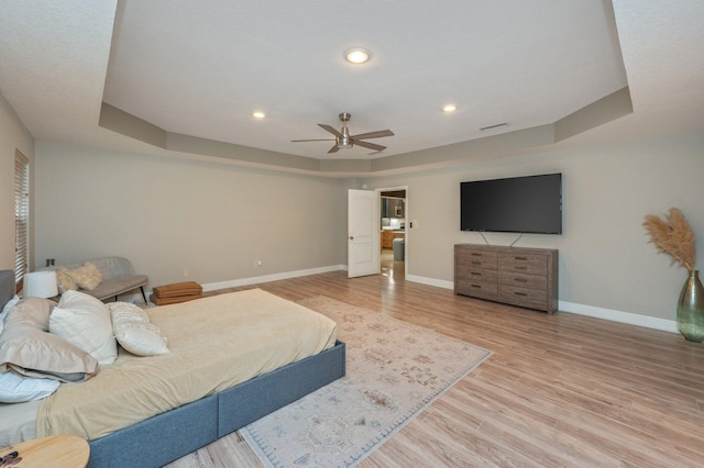 bedroom featuring ceiling fan, a tray ceiling, and light hardwood / wood-style floors