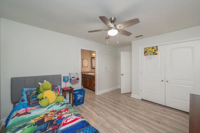 bedroom featuring a textured ceiling, ceiling fan, light hardwood / wood-style floors, a closet, and ensuite bath