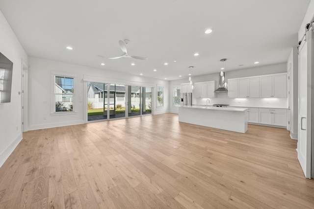 unfurnished living room with plenty of natural light, a barn door, ceiling fan, and light hardwood / wood-style flooring