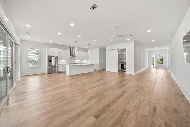 unfurnished living room featuring a barn door, ceiling fan, plenty of natural light, and light hardwood / wood-style flooring