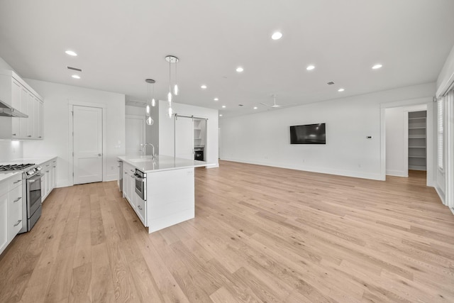 kitchen featuring a kitchen island with sink, white cabinets, light hardwood / wood-style flooring, a barn door, and gas stove