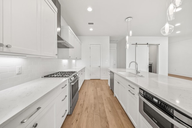 kitchen featuring hanging light fixtures, a barn door, light hardwood / wood-style floors, white cabinets, and appliances with stainless steel finishes