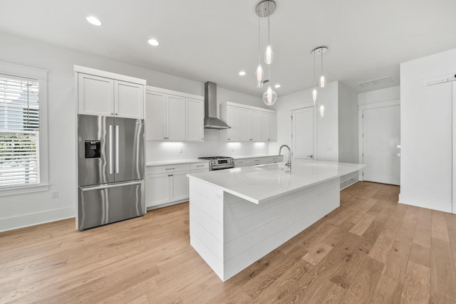 kitchen featuring white cabinets, wall chimney exhaust hood, light hardwood / wood-style floors, and stainless steel appliances