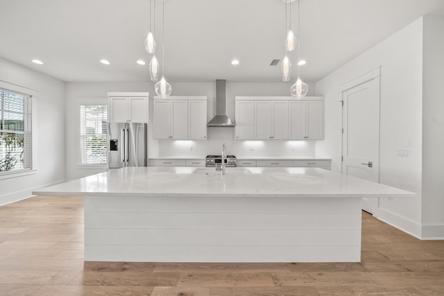 kitchen featuring a large island, wall chimney exhaust hood, high end fridge, and hanging light fixtures