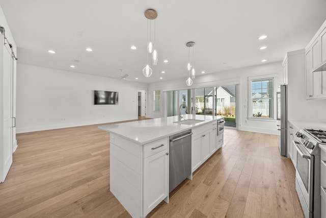 kitchen featuring a kitchen island with sink, white cabinets, stainless steel appliances, and light wood-type flooring