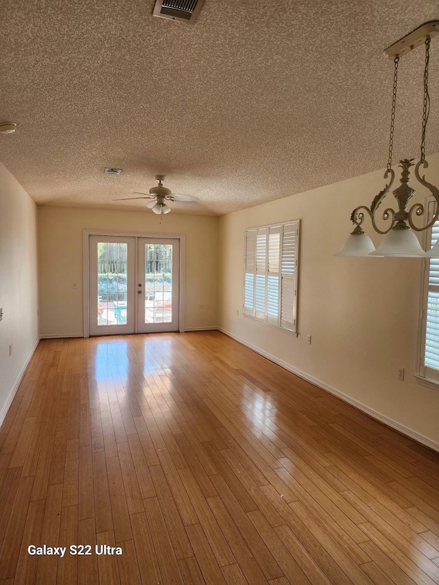 empty room with french doors, a textured ceiling, light hardwood / wood-style flooring, and ceiling fan