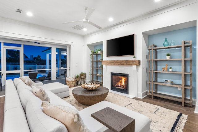 living room featuring dark wood-type flooring, ceiling fan, and a premium fireplace