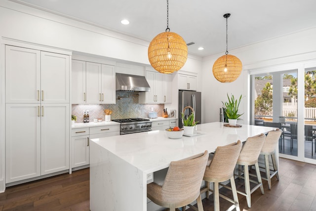 kitchen featuring stainless steel appliances, an island with sink, wall chimney range hood, and white cabinetry