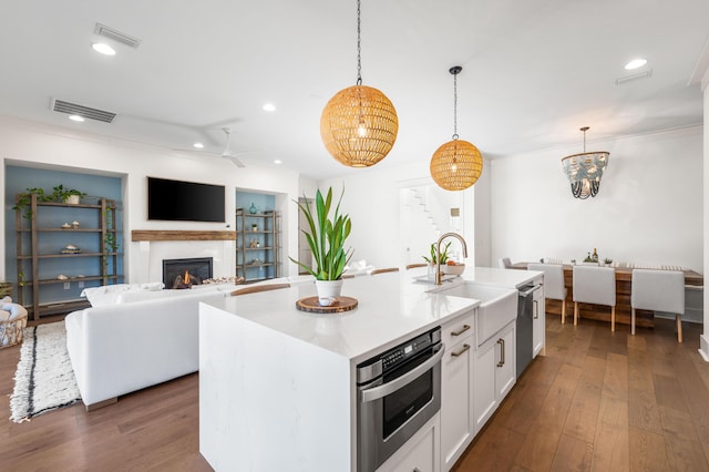 kitchen with a kitchen island with sink, sink, decorative light fixtures, and white cabinetry