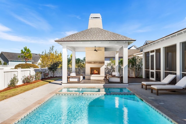 view of swimming pool featuring a pool with connected hot tub, a patio, a warm lit fireplace, a fenced backyard, and a gazebo