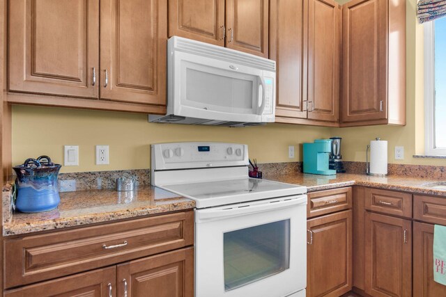 kitchen featuring white appliances, brown cabinetry, and light stone countertops