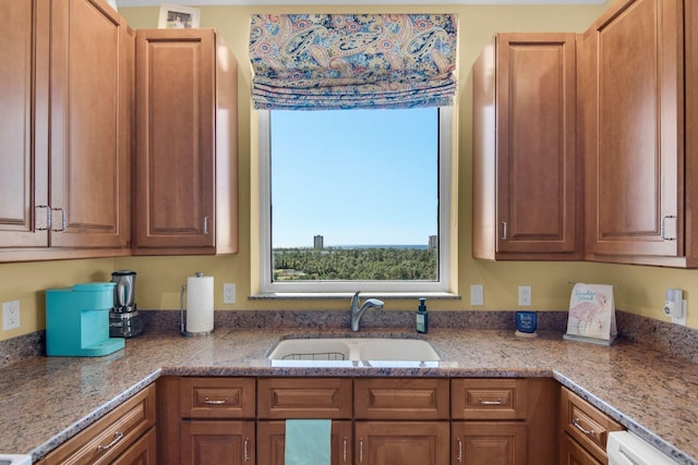 kitchen with light stone counters, brown cabinets, and a sink