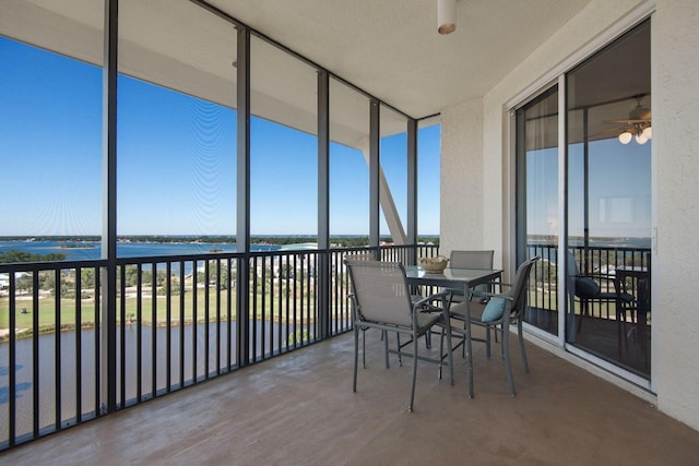 unfurnished sunroom featuring a ceiling fan, a water view, and a wealth of natural light