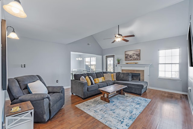 living room featuring ceiling fan with notable chandelier, dark hardwood / wood-style floors, high vaulted ceiling, and a tiled fireplace