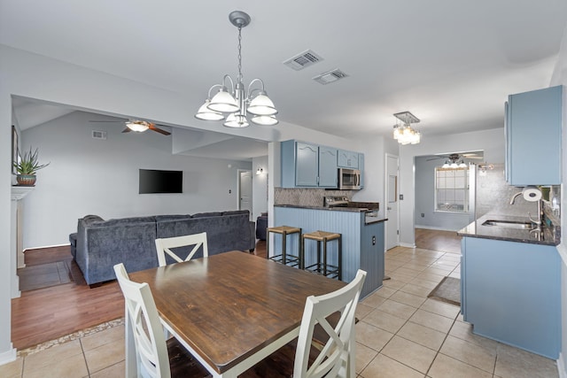 dining space with vaulted ceiling, sink, ceiling fan with notable chandelier, and light wood-type flooring