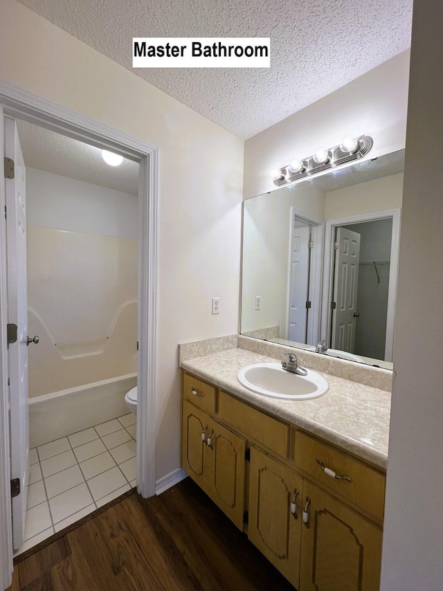 full bathroom with a textured ceiling, toilet, shower / washtub combination, vanity, and hardwood / wood-style flooring