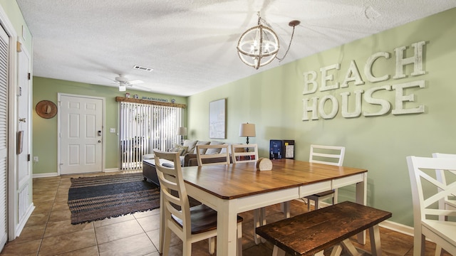 tiled dining area with a textured ceiling and ceiling fan with notable chandelier