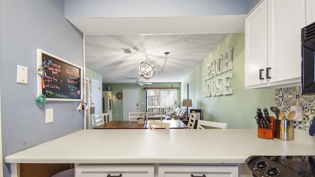 kitchen with kitchen peninsula, a textured ceiling, ceiling fan with notable chandelier, decorative light fixtures, and white cabinetry