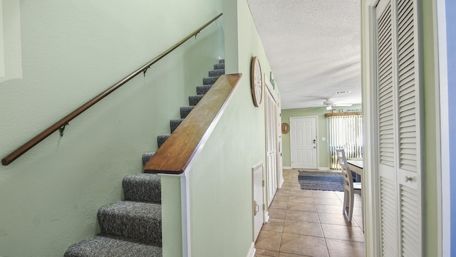 staircase featuring tile patterned flooring, ceiling fan, and a textured ceiling