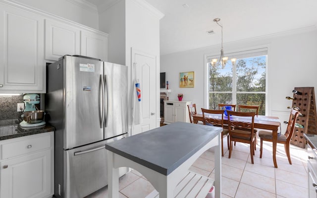 kitchen with white cabinetry, crown molding, decorative light fixtures, light tile patterned floors, and stainless steel refrigerator