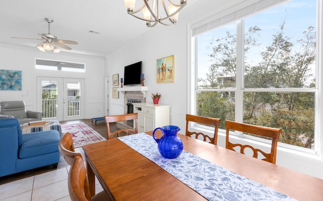 tiled dining room with french doors, ornamental molding, and ceiling fan with notable chandelier