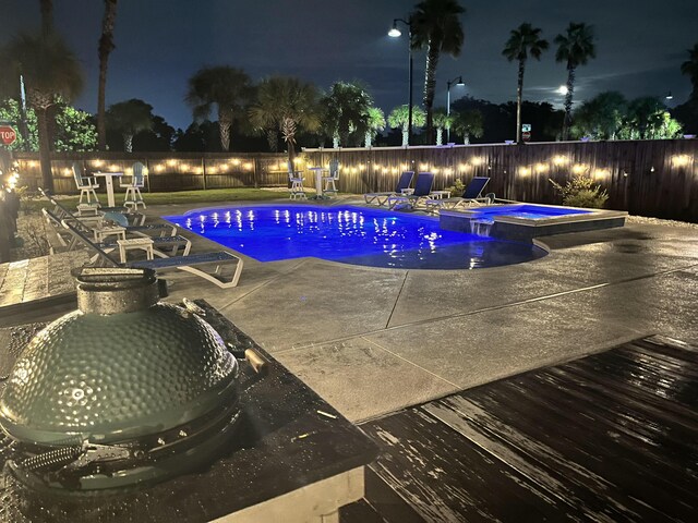 pool at twilight with an in ground hot tub and a patio area