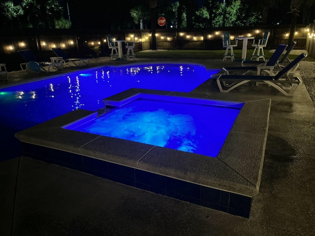 pool at twilight featuring an in ground hot tub and a patio