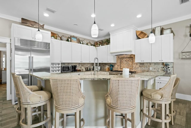 kitchen with white cabinetry, dark wood-type flooring, hanging light fixtures, stainless steel appliances, and a kitchen breakfast bar