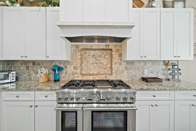 kitchen with decorative backsplash, light stone countertops, custom range hood, double oven range, and white cabinetry