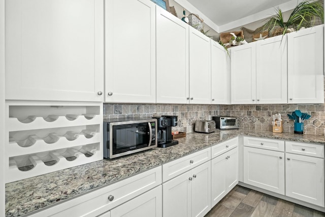 kitchen featuring tasteful backsplash, white cabinetry, light stone counters, and hardwood / wood-style flooring