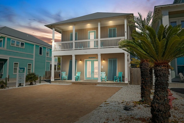 back house at dusk with a balcony, covered porch, and french doors