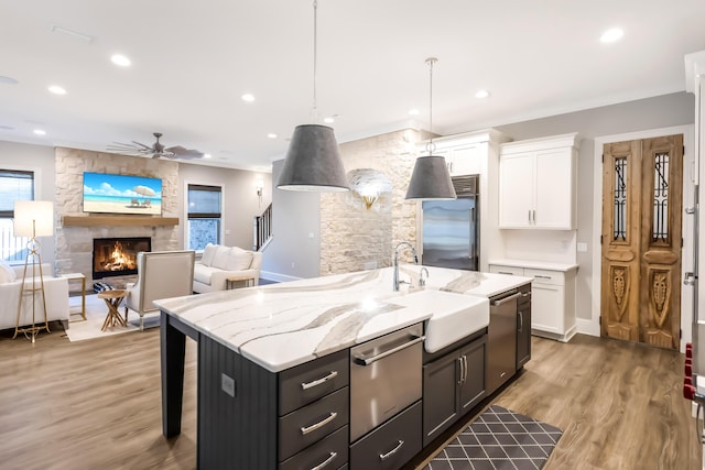 kitchen with stainless steel appliances, a kitchen island with sink, decorative light fixtures, white cabinetry, and a stone fireplace