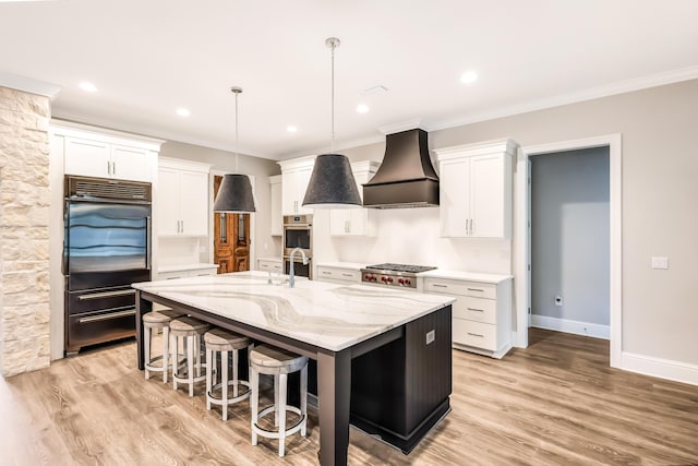 kitchen featuring white cabinets, light hardwood / wood-style floors, premium range hood, and a kitchen island with sink