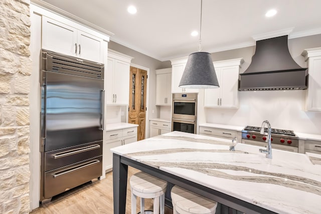 kitchen with white cabinets, appliances with stainless steel finishes, premium range hood, and hanging light fixtures