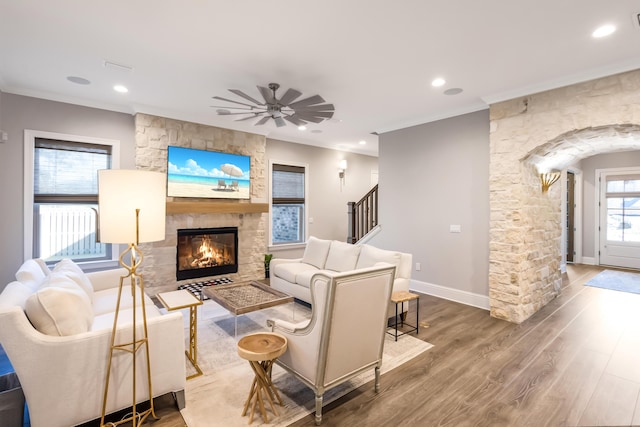 living room with ceiling fan, wood-type flooring, a fireplace, and ornamental molding