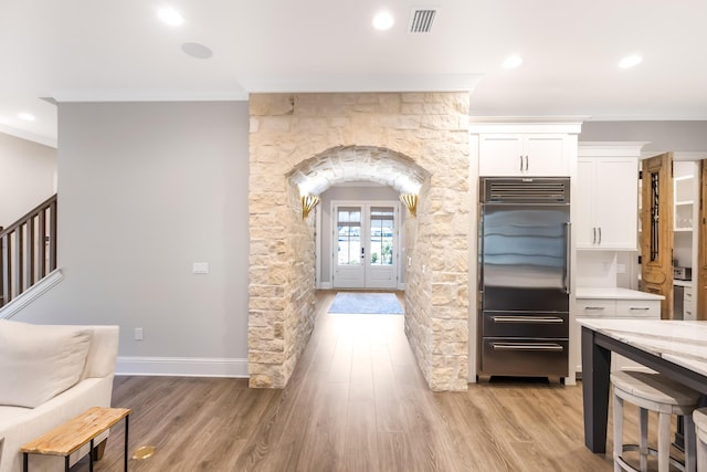 kitchen featuring stainless steel built in refrigerator, light hardwood / wood-style flooring, white cabinetry, and crown molding