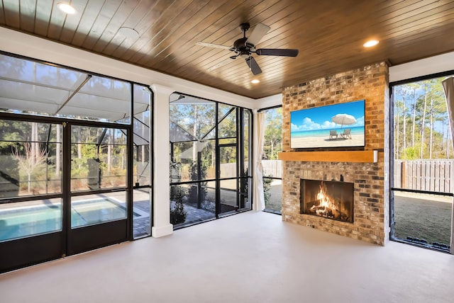 unfurnished sunroom with ceiling fan, wooden ceiling, and a fireplace