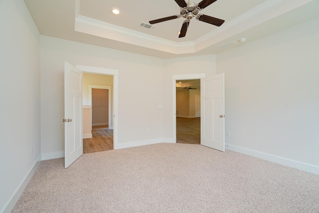 unfurnished bedroom featuring a walk in closet, ceiling fan, a tray ceiling, light colored carpet, and a closet