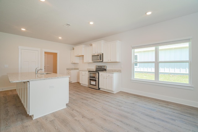 kitchen with a kitchen island with sink, sink, appliances with stainless steel finishes, light hardwood / wood-style floors, and white cabinetry