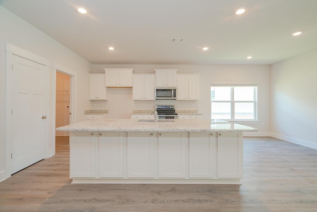 kitchen with a center island with sink, white cabinets, and light stone counters