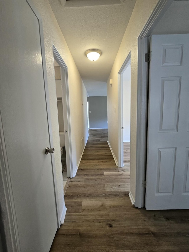 corridor with a textured ceiling and dark wood-type flooring