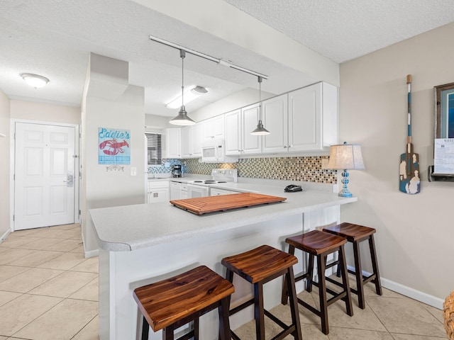 kitchen featuring a kitchen bar, kitchen peninsula, white cabinets, and white appliances