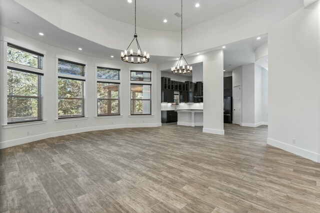 unfurnished living room with a towering ceiling, a chandelier, and light wood-type flooring