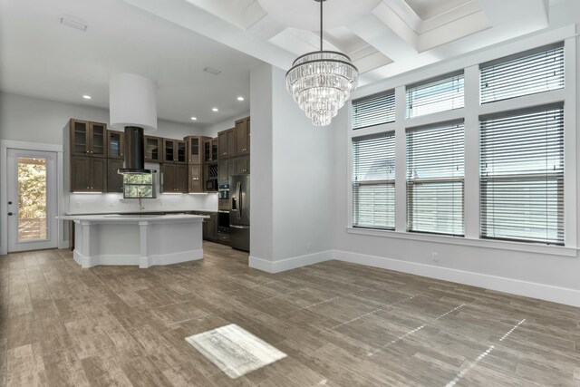 kitchen featuring dark brown cabinets, coffered ceiling, ventilation hood, a kitchen island, and decorative light fixtures