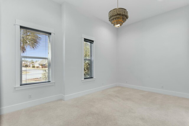 carpeted empty room featuring an inviting chandelier