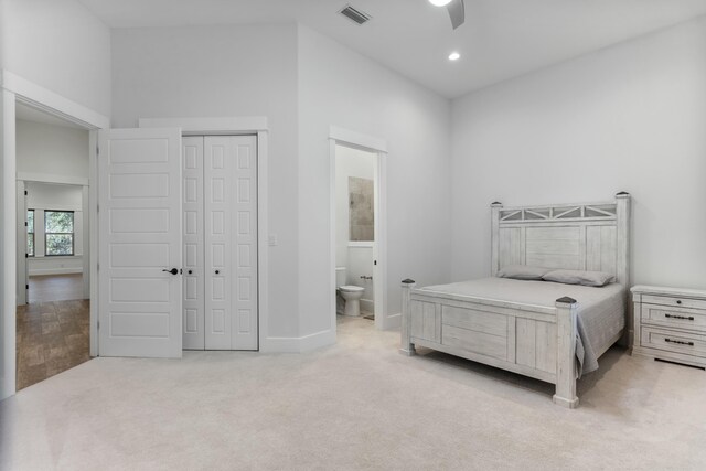 bedroom with connected bathroom, light colored carpet, ceiling fan, and a closet