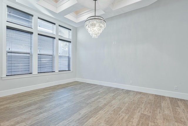 spare room with an inviting chandelier, coffered ceiling, light hardwood / wood-style flooring, and beamed ceiling