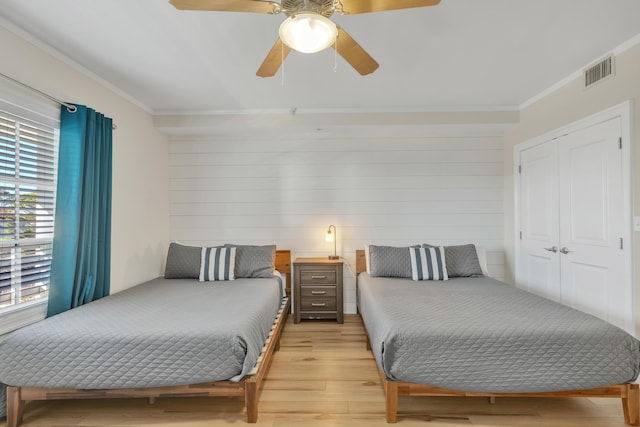 bedroom with ceiling fan, light hardwood / wood-style flooring, crown molding, and wood walls