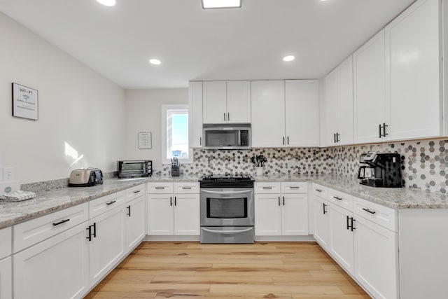 kitchen with white cabinets, appliances with stainless steel finishes, decorative backsplash, and light stone counters