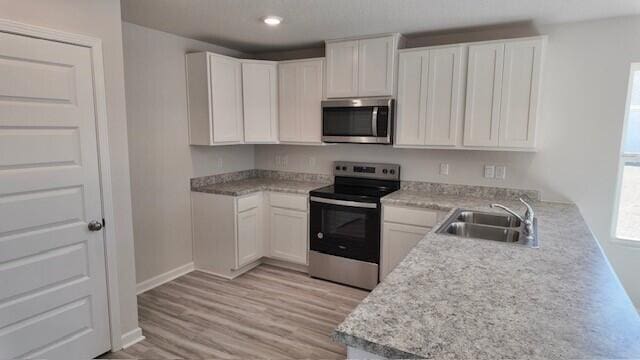 kitchen featuring a wealth of natural light, white cabinetry, sink, light hardwood / wood-style flooring, and appliances with stainless steel finishes